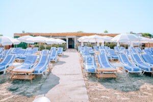 Rang&eacute;e de transats bleus et parasols blancs sur le sable de La R&eacute;serve Plage au Grau du Roi