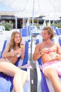Jeune couple souriant sur des transats avec cocktails &agrave; La R&eacute;serve Plage, Grau du Roi